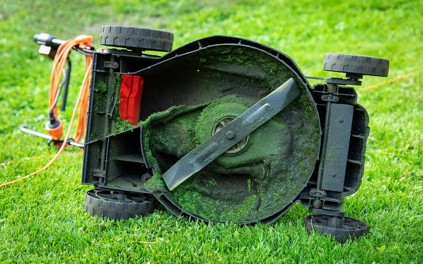 A lawn mower on its side showing the blade on its underside.