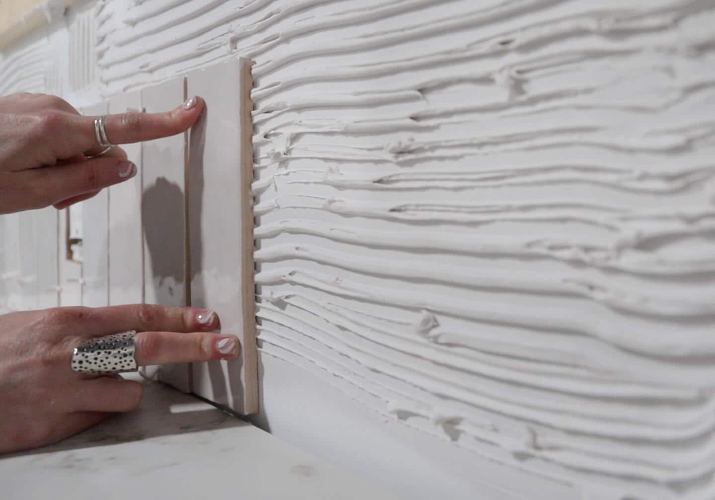  Girl hands with silver rings pressing white tile into white paste. 