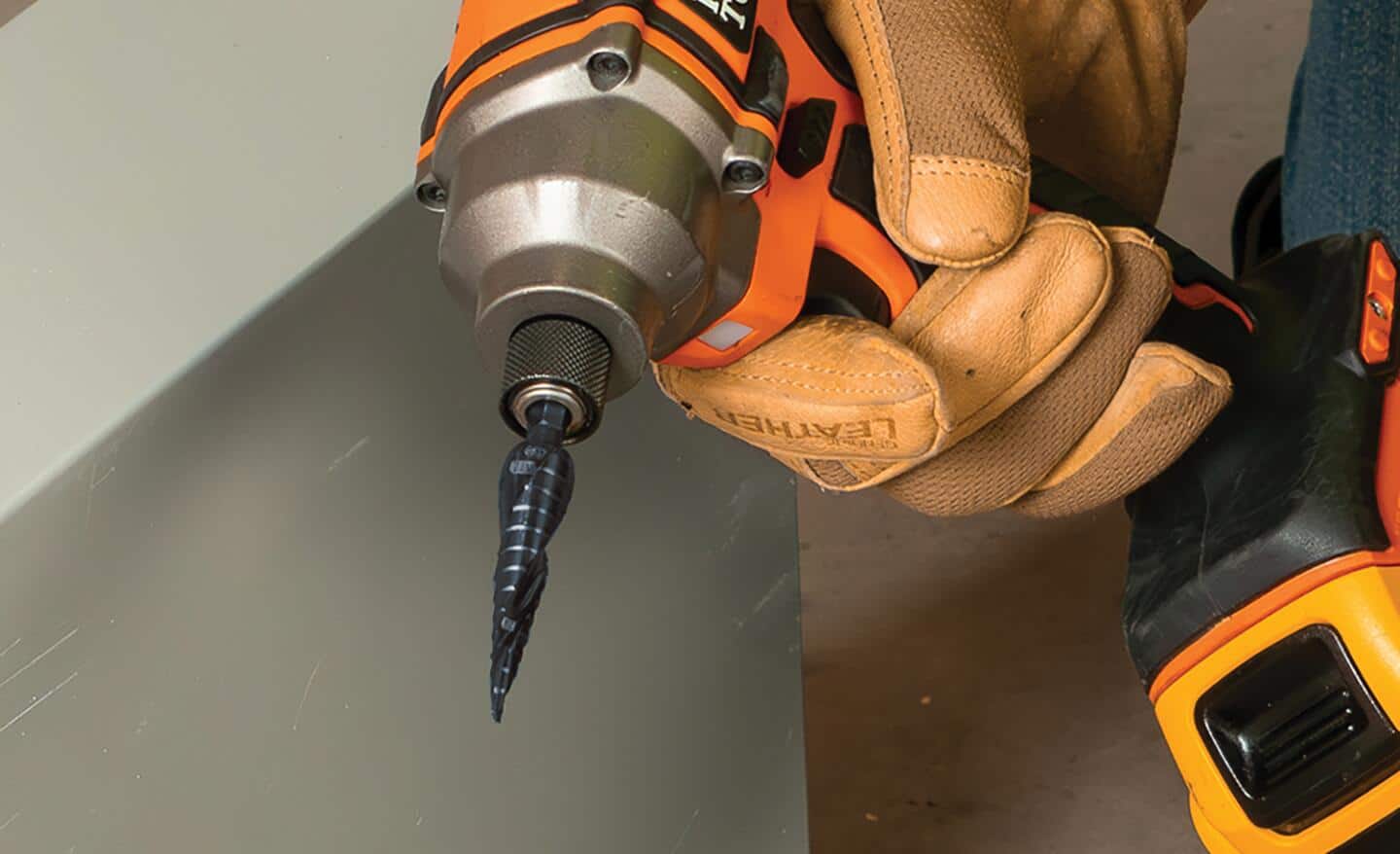 A person holding an orange drill with a step drill bit.