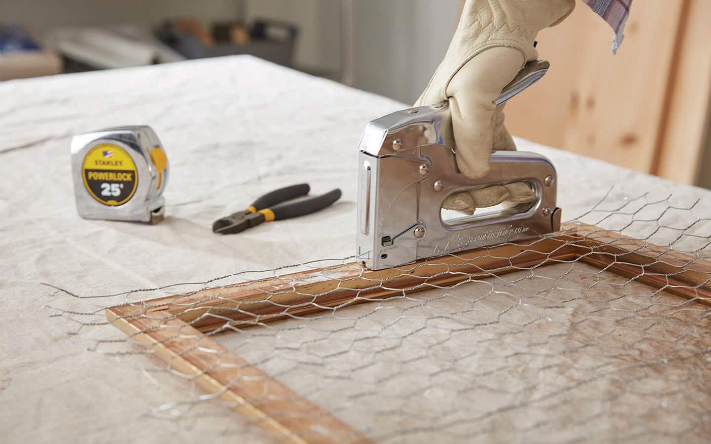A person uses a hand stapler to attach chicken wire to a frame. A person uses a hand stapler to attach chicken wire to a frame.