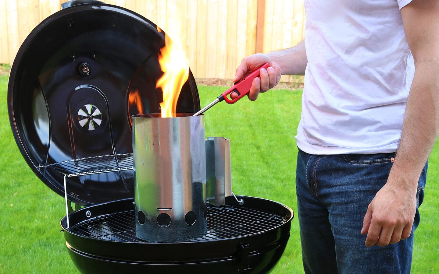 A person lights coals in a charcoal chimney with a lighter. A person lights coals in a charcoal chimney with a lighter.