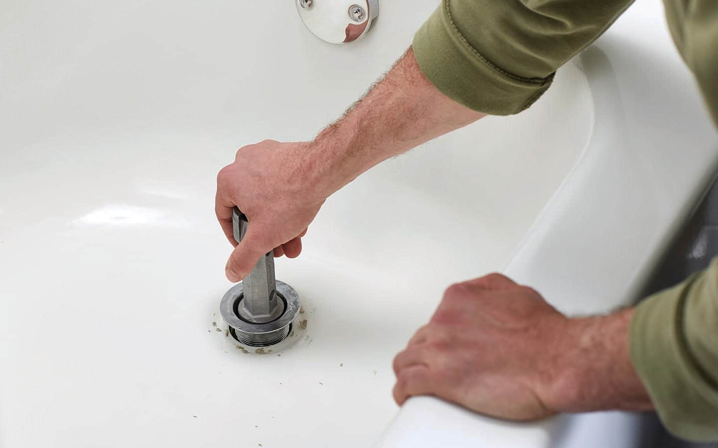 A drain basket being carefully removed from a bathtub.