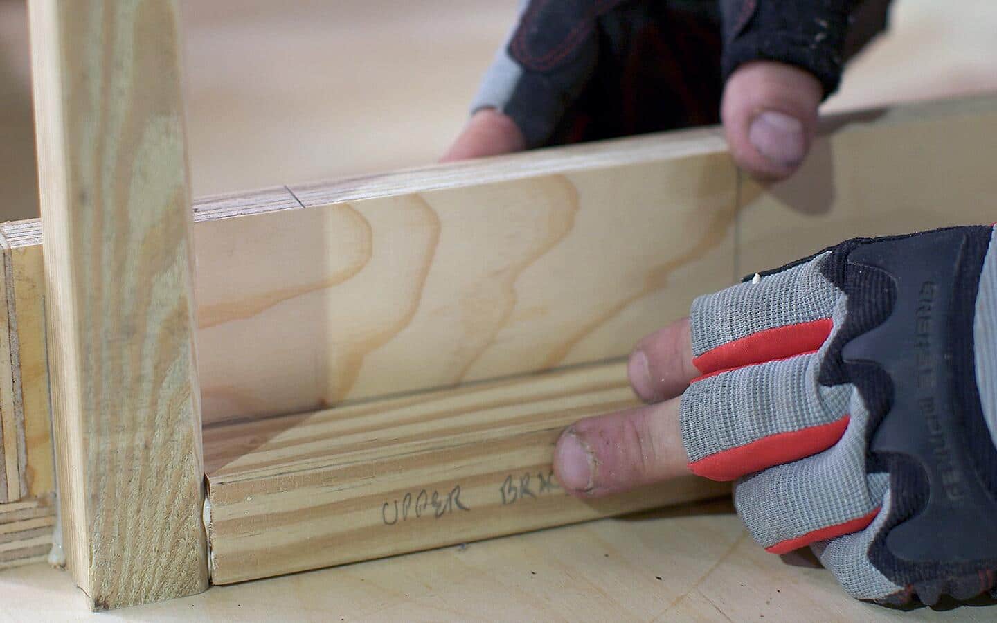 A gloved individual attaching plywood pieces together for a DIY desk.
