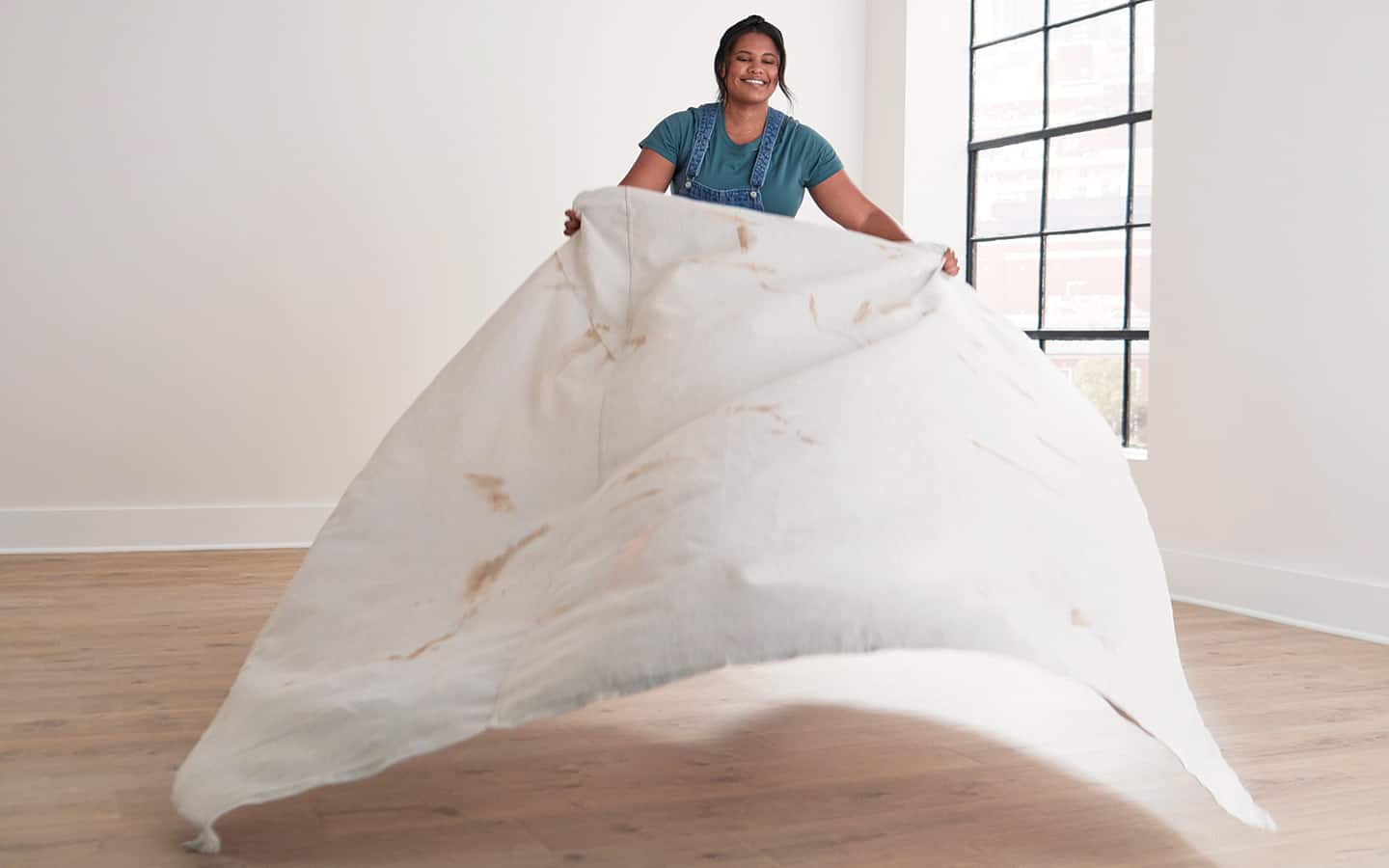 A person spreading a drop cloth over a floor.