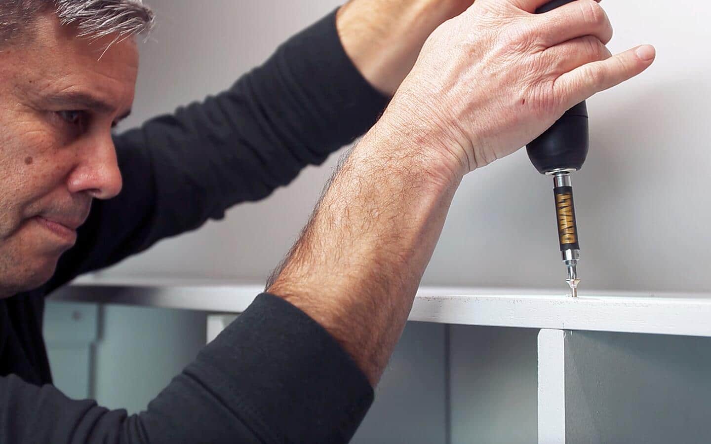 A man drilling a lower shelf into place on top of shelf supports.