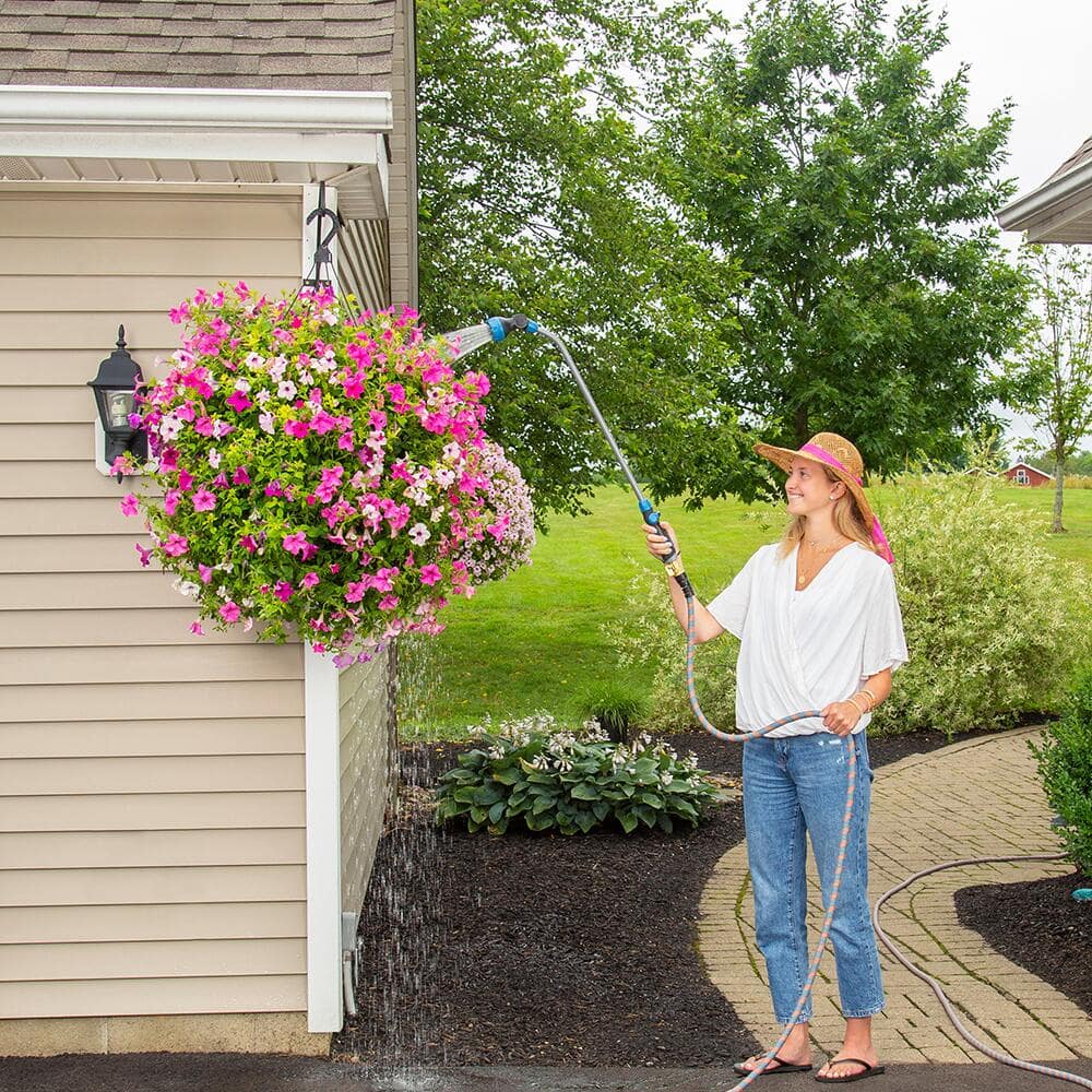 Gardener using a watering wand to water a hanging basket with pink flowers