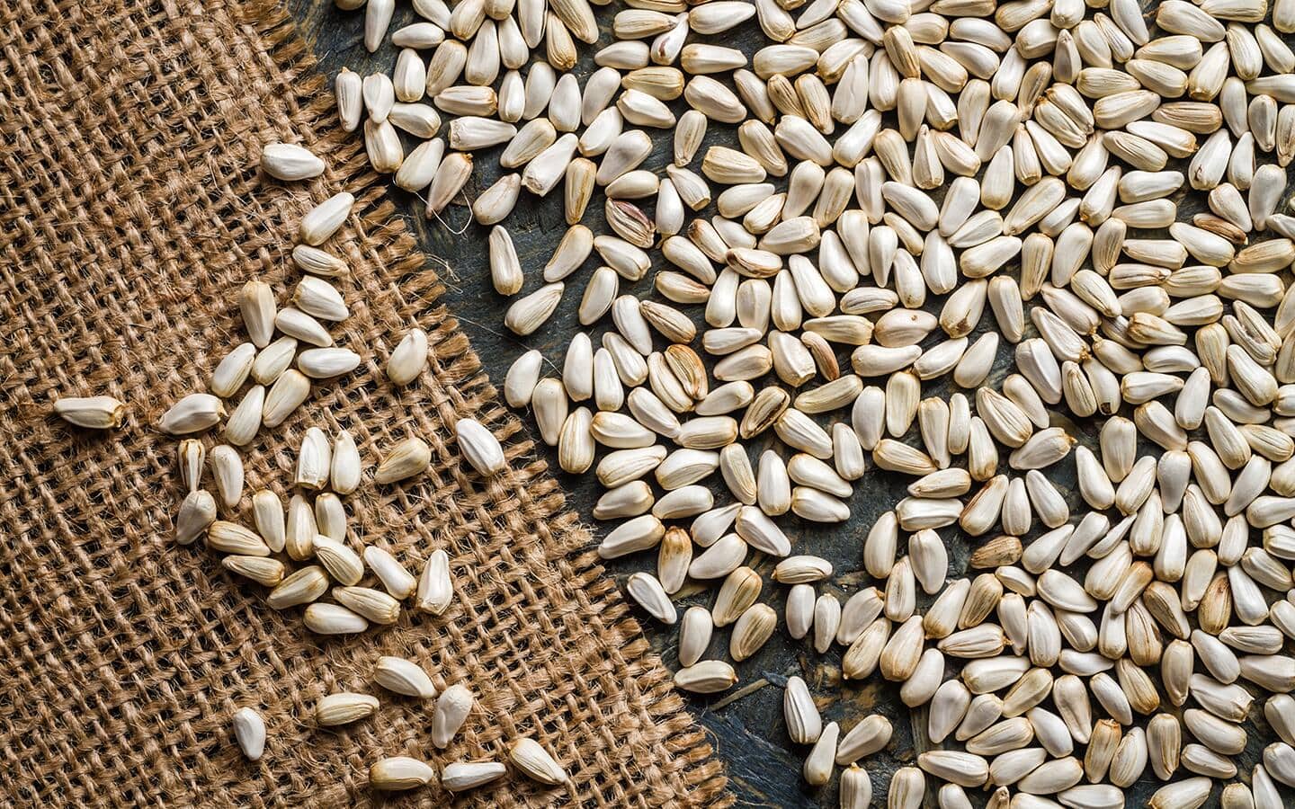 A pile of safflower seeds on a burlap and wood surface.