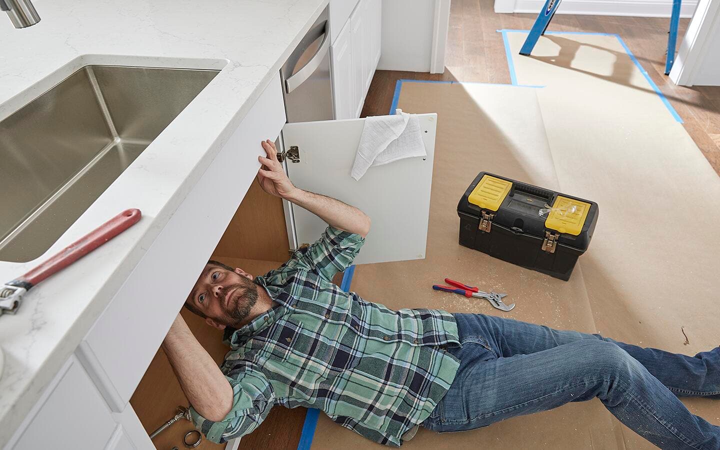 A person on their back reconnecting the water supply lines for a new kitchen sink.  A person on their back reconnecting the water supply lines for a new kitchen sink.
