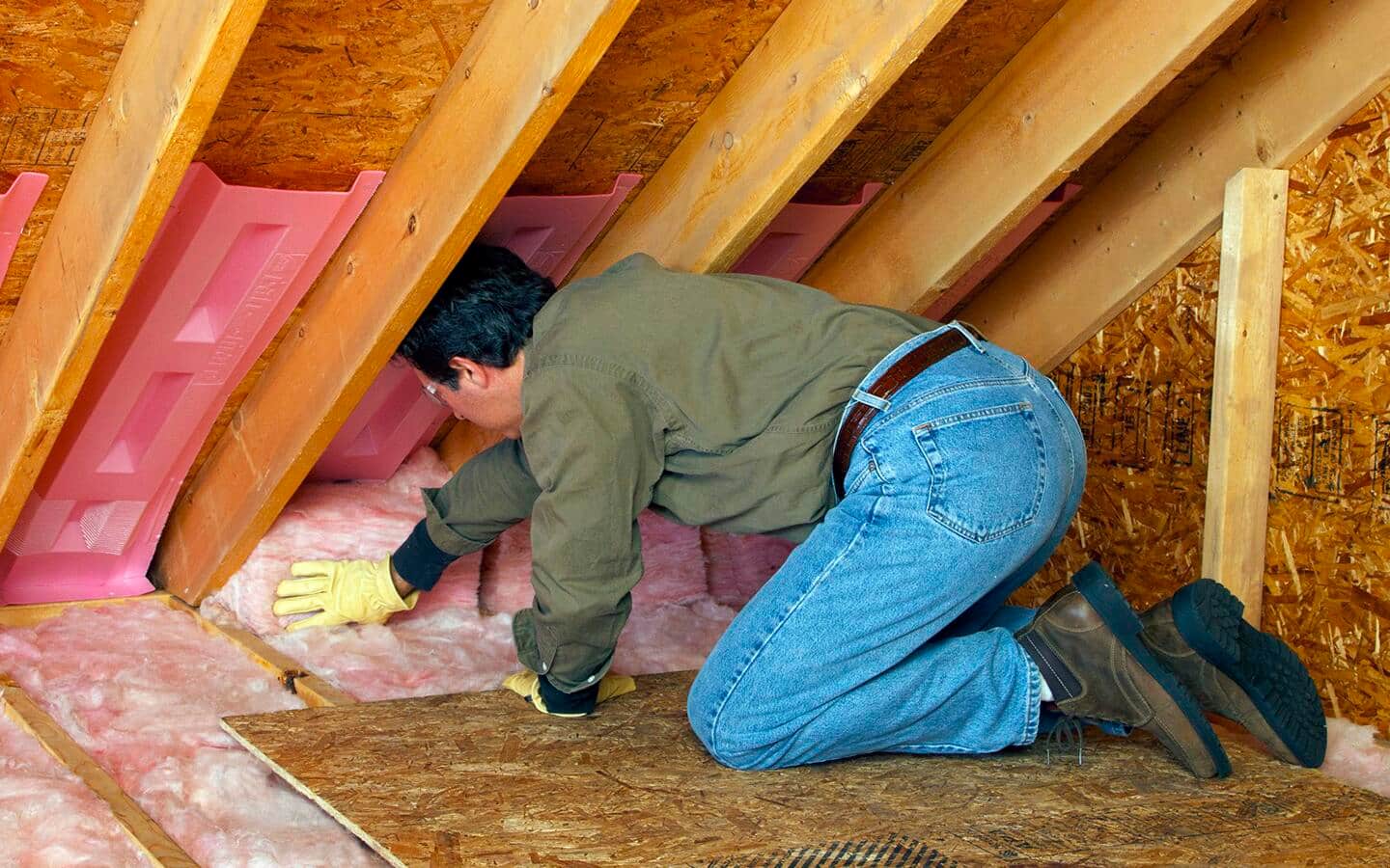 A man installs insulation in an attic. A man installs insulation in an attic.