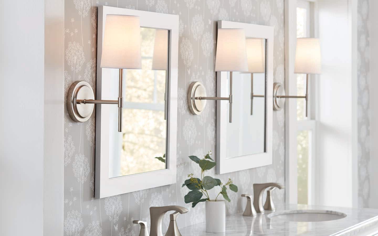 Lamps on hanging wall sconces surrounding a pair of vanity mirrors in a bathroom. Lamps on hanging wall sconces surrounding a pair of vanity mirrors in a bathroom.