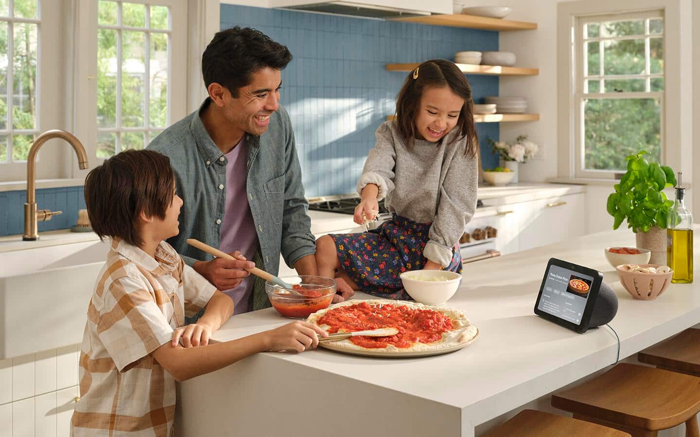 An adult and two children using a smart hub on a kitchen island to prepare a pizza. An adult and two children using a smart hub on a kitchen island to prepare a pizza.