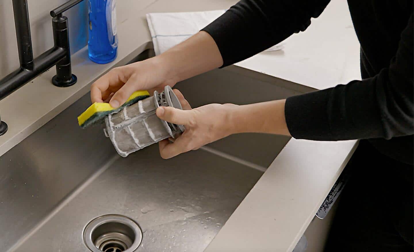 A person washing the dishwasher filter in a sink.