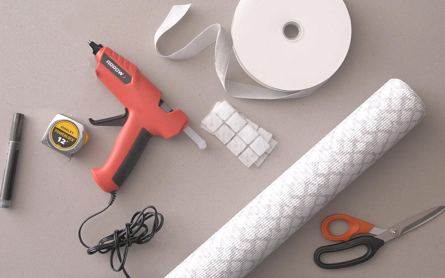 Shelf liner, a hot glue gun, a marker and other items sit on a counter.