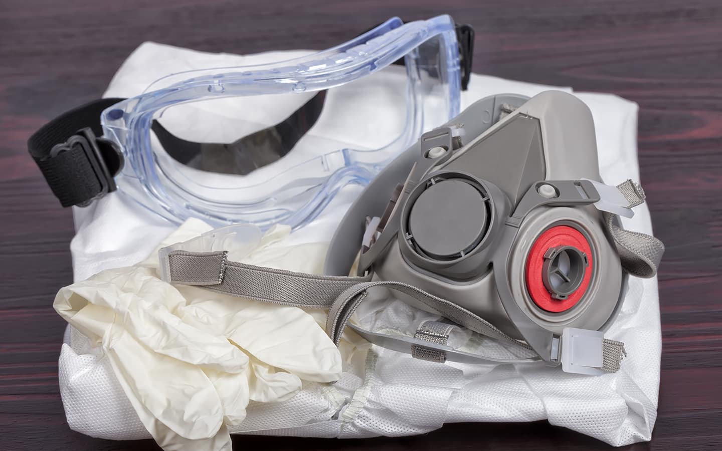 Safety goggles, gloves and a respirator sitting on top of folded white paint coveralls.