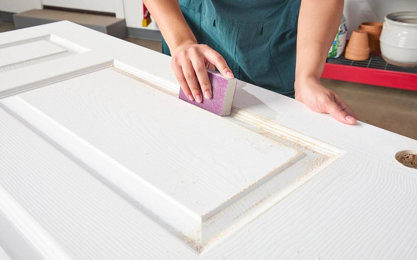 A woman uses a sanding block to prepare a raised panel door for painting. A woman uses a sanding block to prepare a raised panel door for painting.