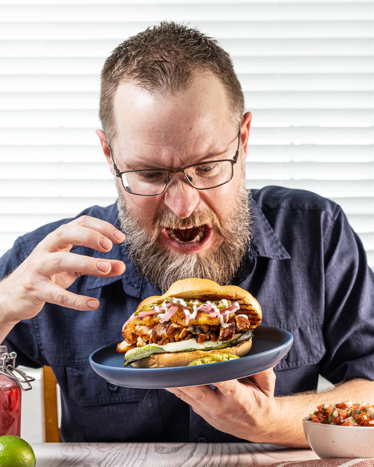 A man growling at a grilled chicken torta on a plate. A man growling at a grilled chicken torta on a plate.