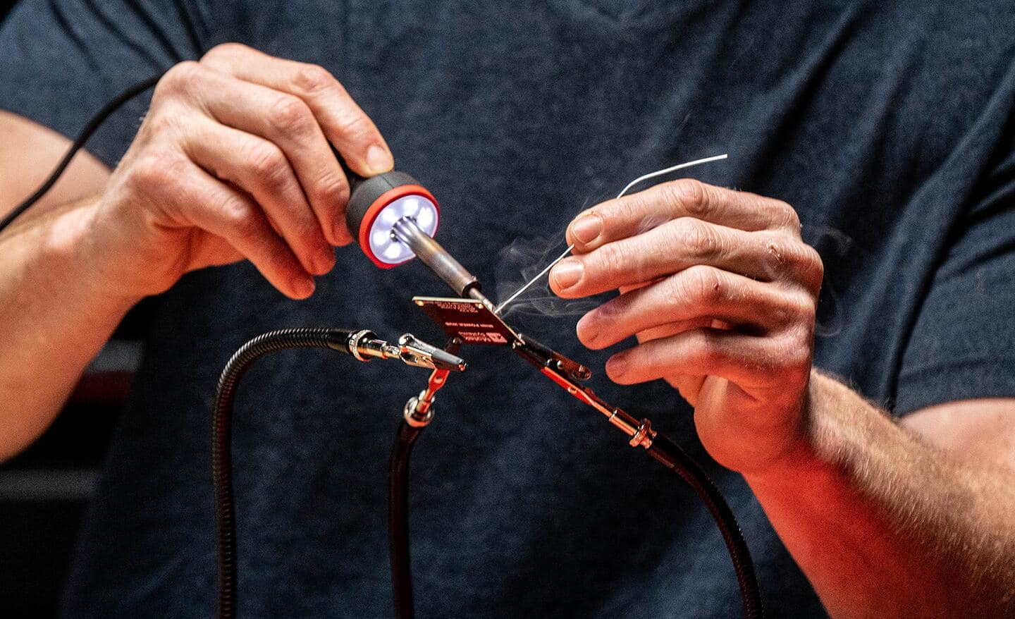 A man uses a soldering iron to make a connection on a small circuit board.