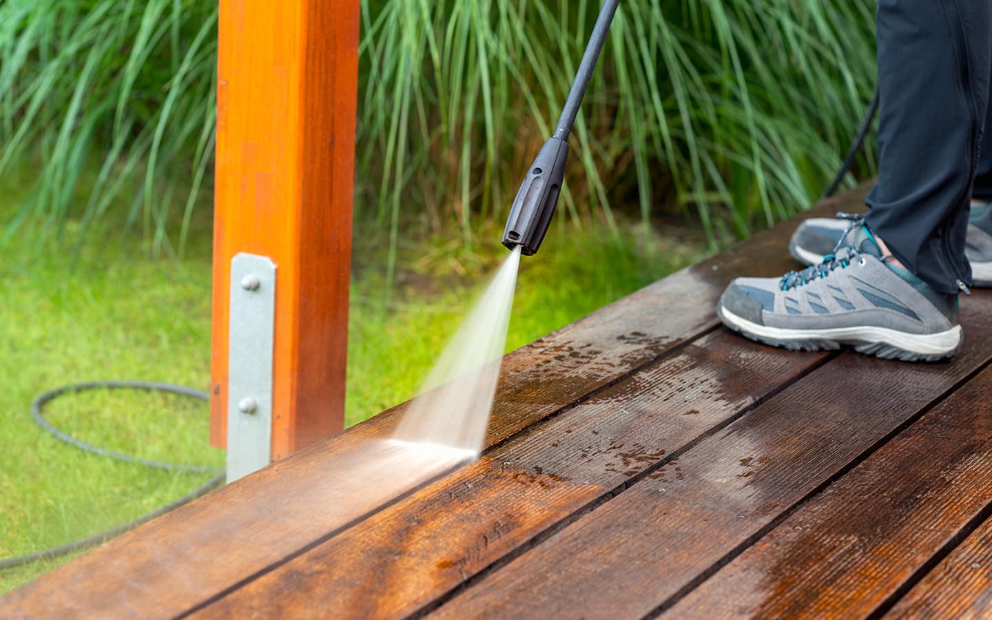 Person directs a stream of water from a pressure washer onto a wood deck