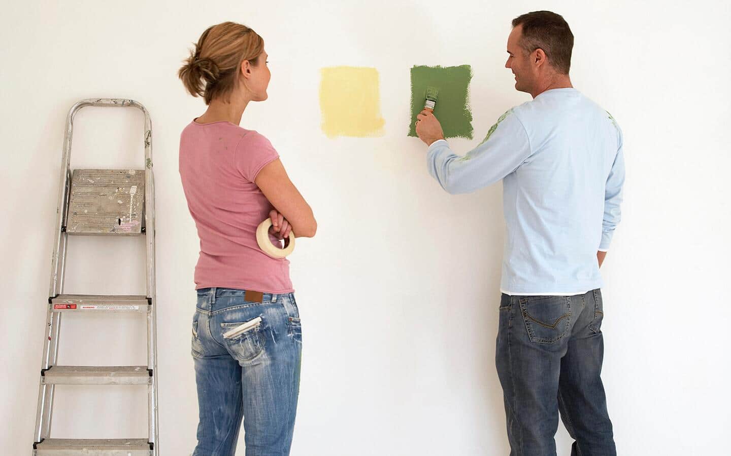 A ladder rests against a wall featuring large test paint squares of different colors. A ladder rests against a wall featuring large test paint squares of different colors.