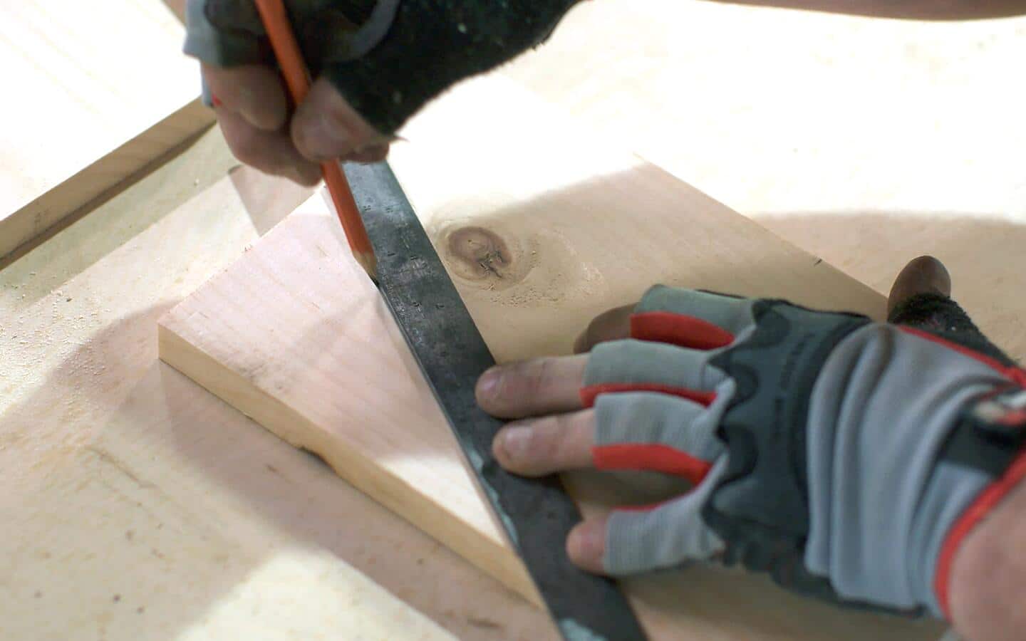 Someone using a pencil and ruler to mark a cut line on a piece of wood to build a birdhouse.