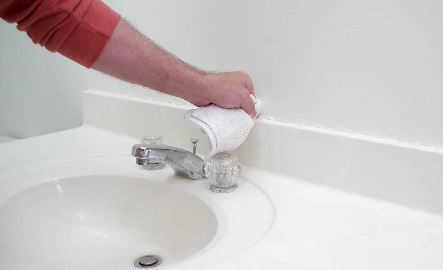 A person wipes away excess caulk on a bathroom vanity.