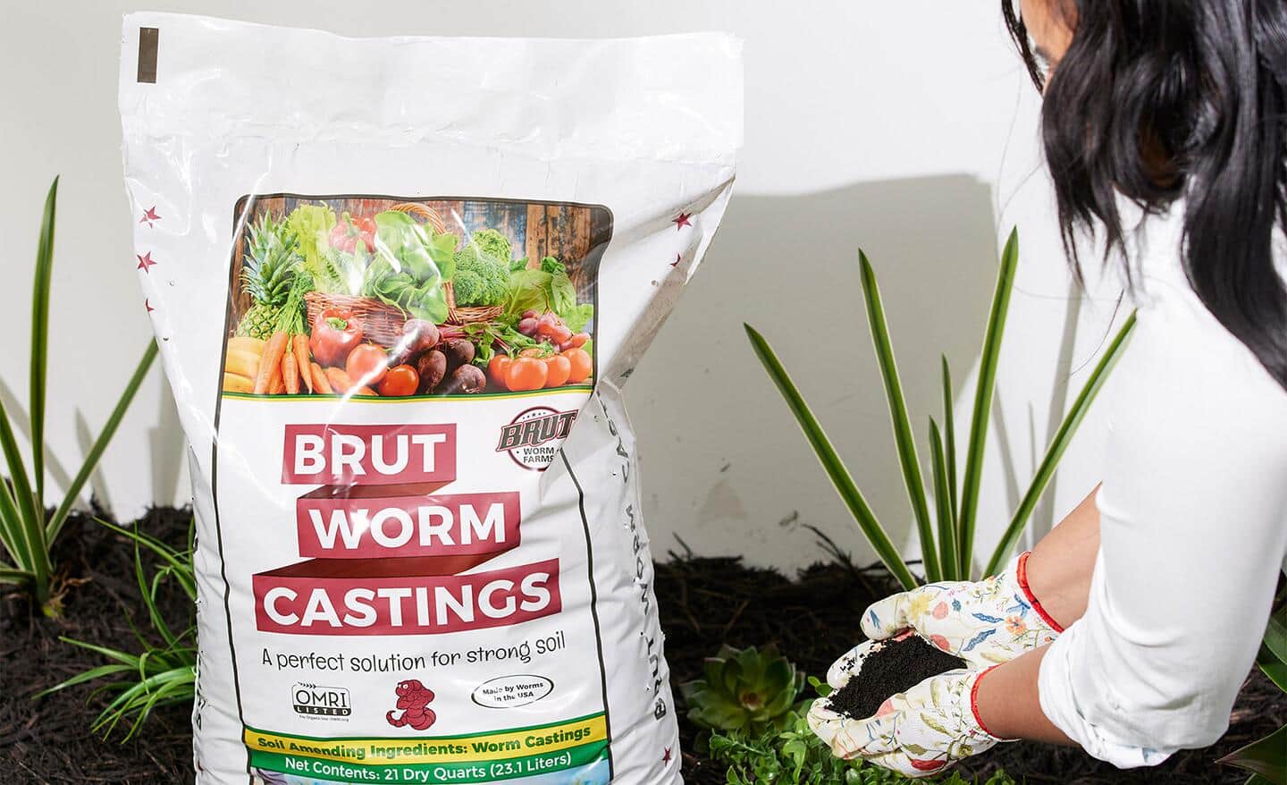 A person next to a bag of worm castings adds soil amendments into a garden.