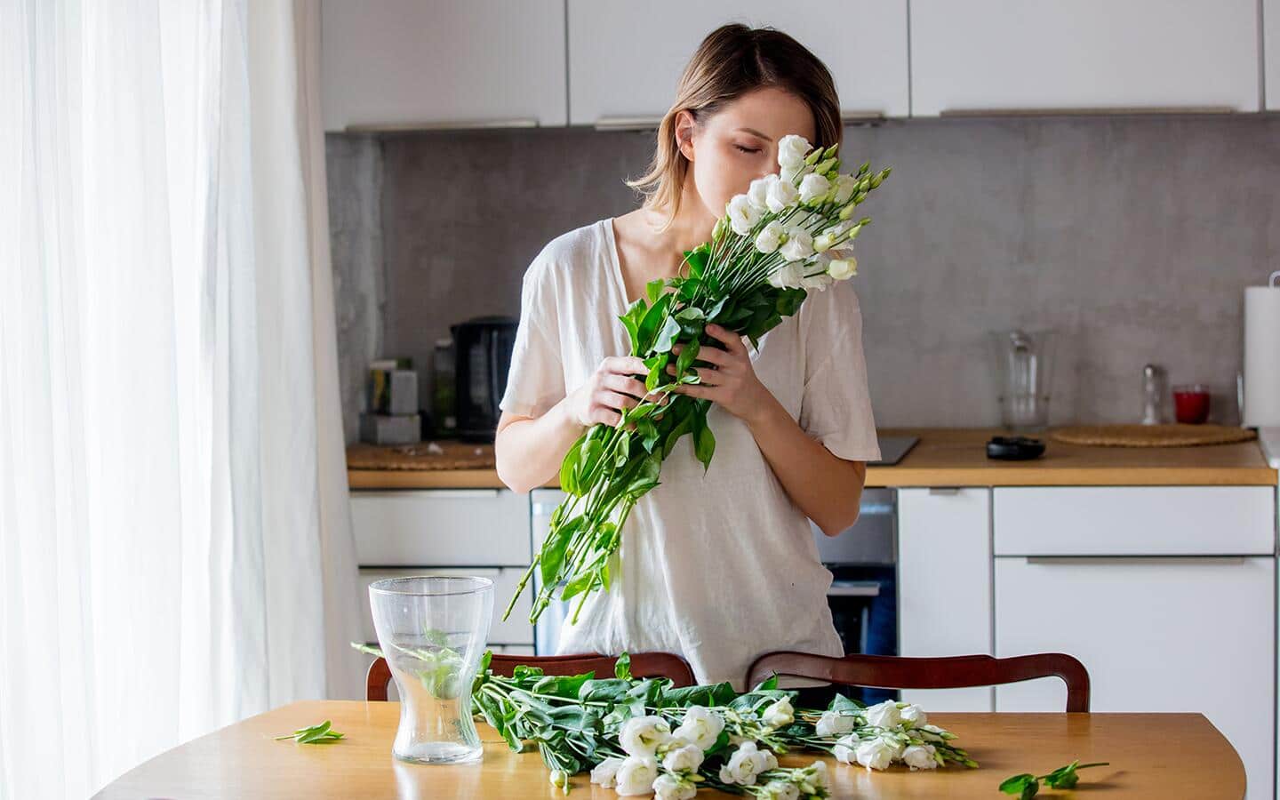 A woman holds a bunch of white roses up to her nose before putting them in a vase.