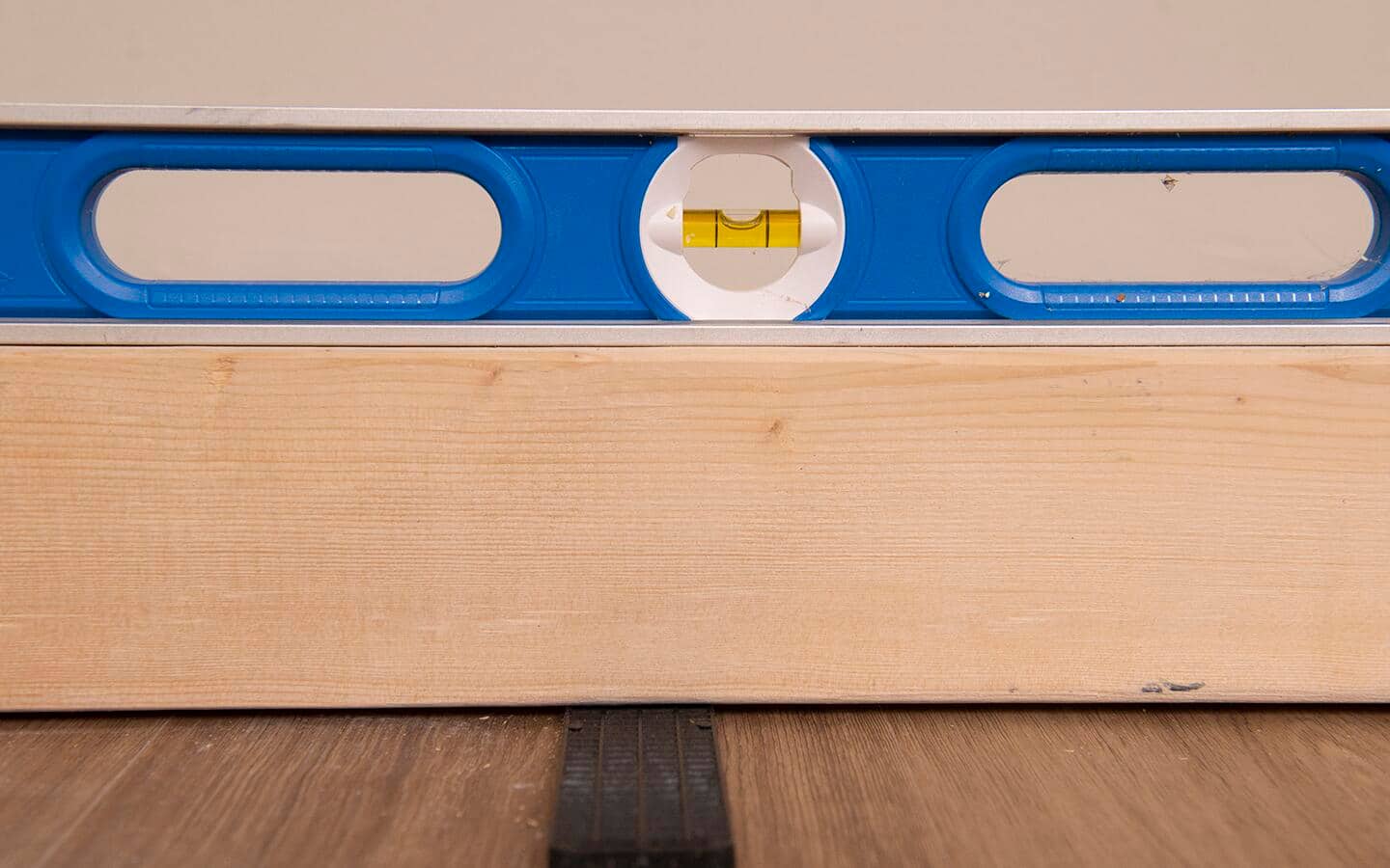 A level and shim being used to adjust the base of a built in shelving unit.