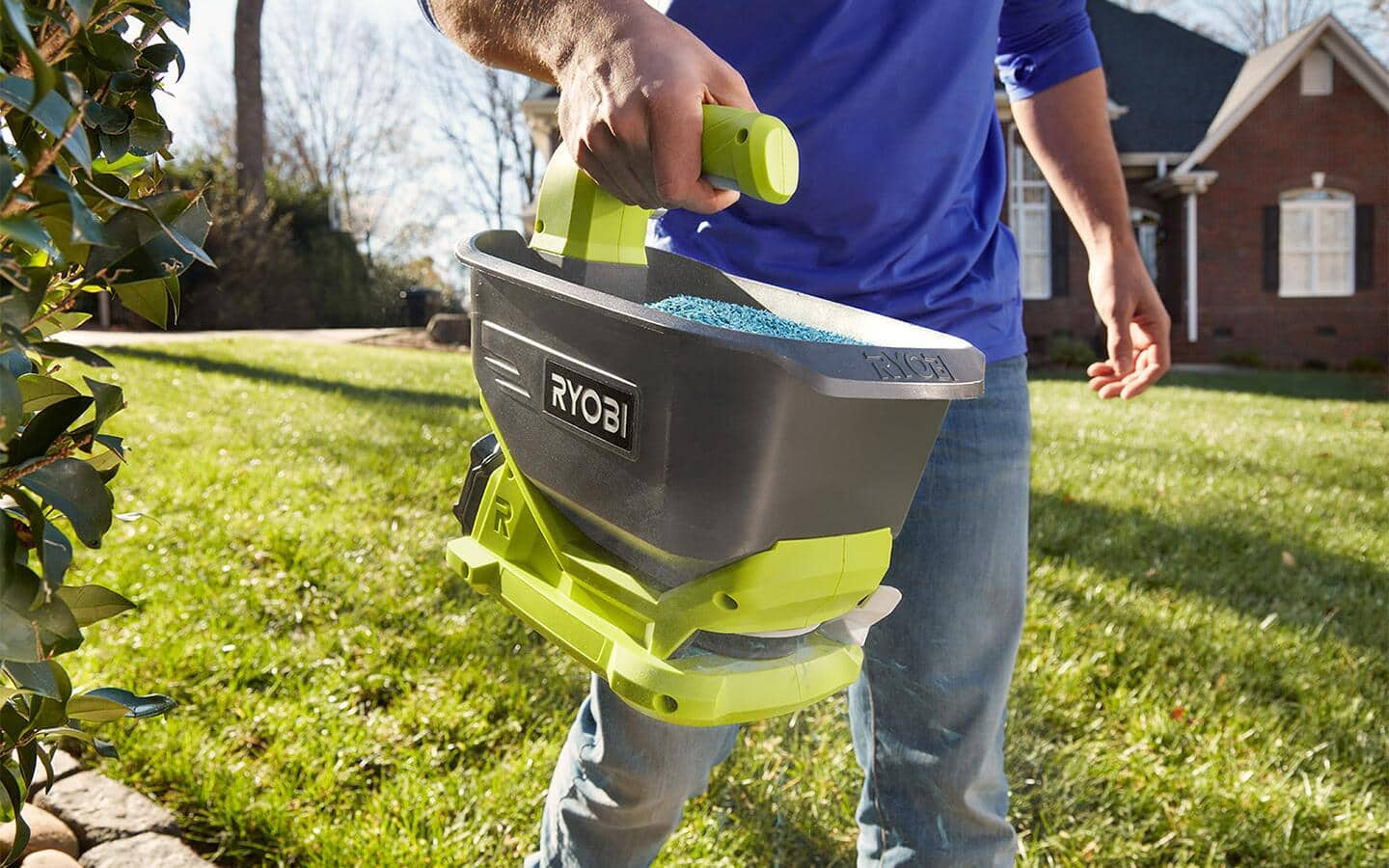 A person uses a handheld spreader to fertilize a lawn. A person uses a handheld spreader to fertilize a lawn.