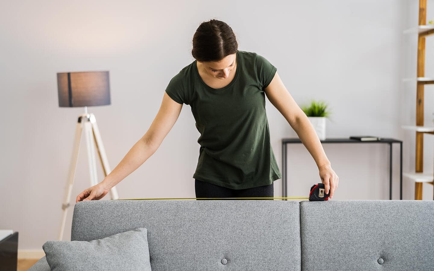 Someone measuring the top of a couch cushion with a tape measure. Someone measuring the top of a couch cushion with a tape measure.