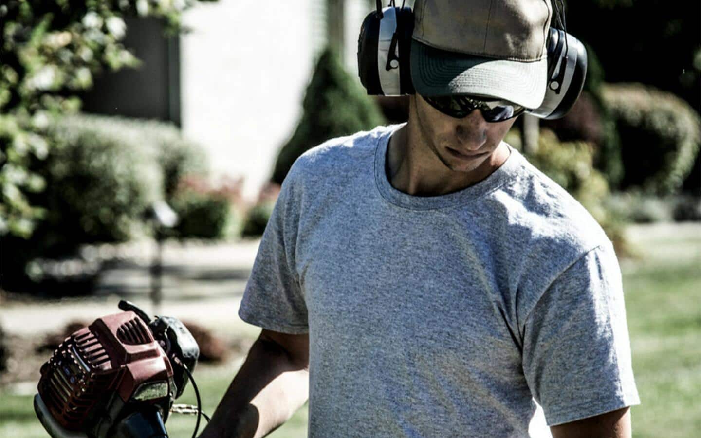 A man wears safety glasses and ear muffs while running a string trimmer. A man wears safety glasses and ear muffs while running a string trimmer.