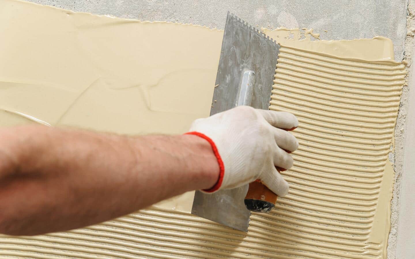 A person creates grooves in a spread of wood adhesive on a floor. A person creates grooves in a spread of wood adhesive on a floor.