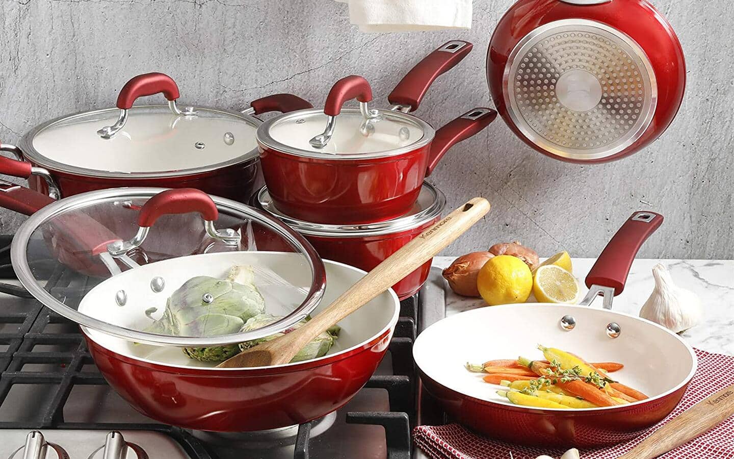 A full ceramic cookware set with glass lids placed on a stovetop.