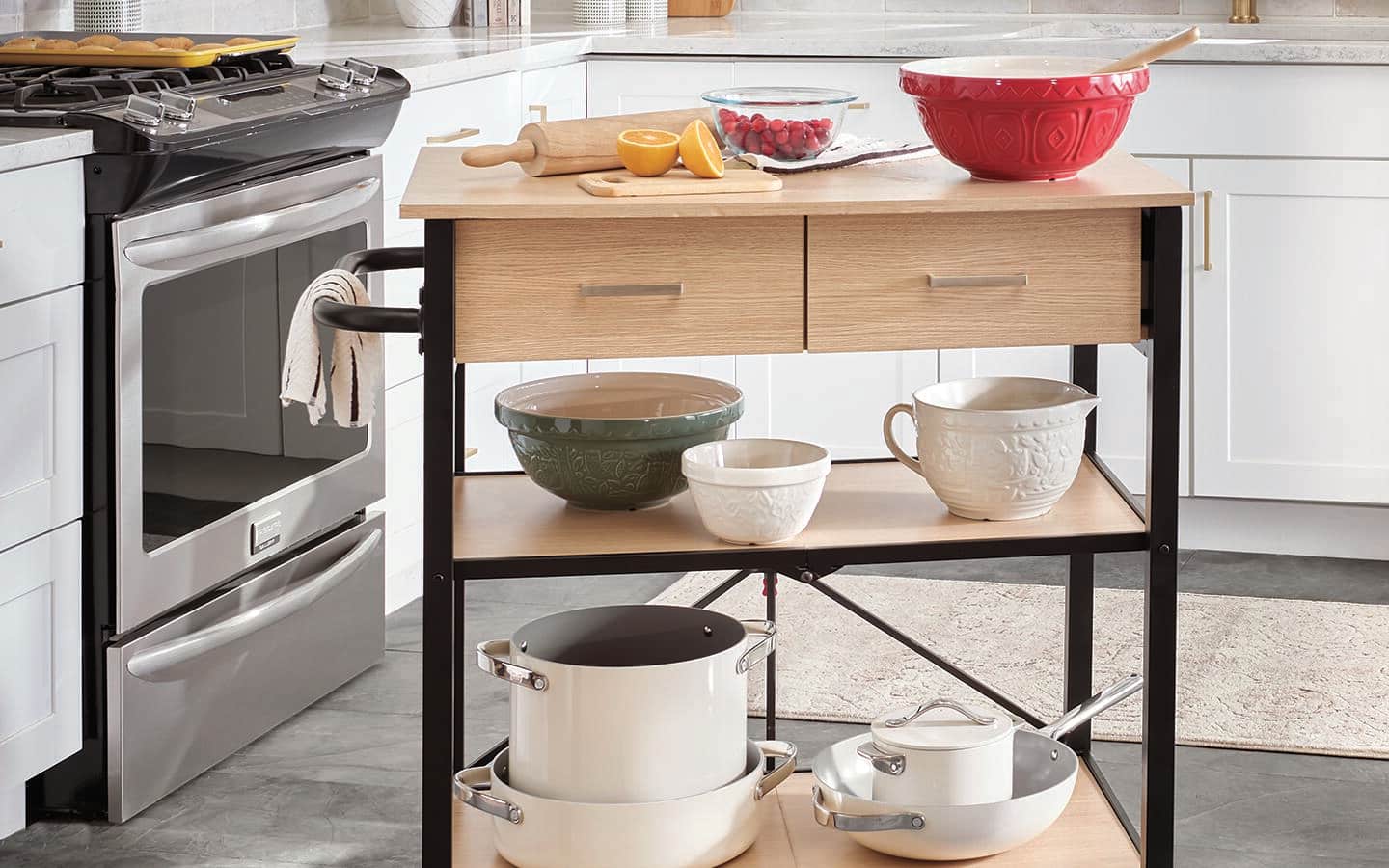 A collection of kitchen tools, pots and mixing bowls placed on a rolling kitchen cart. A collection of kitchen tools, pots and mixing bowls placed on a rolling kitchen cart.