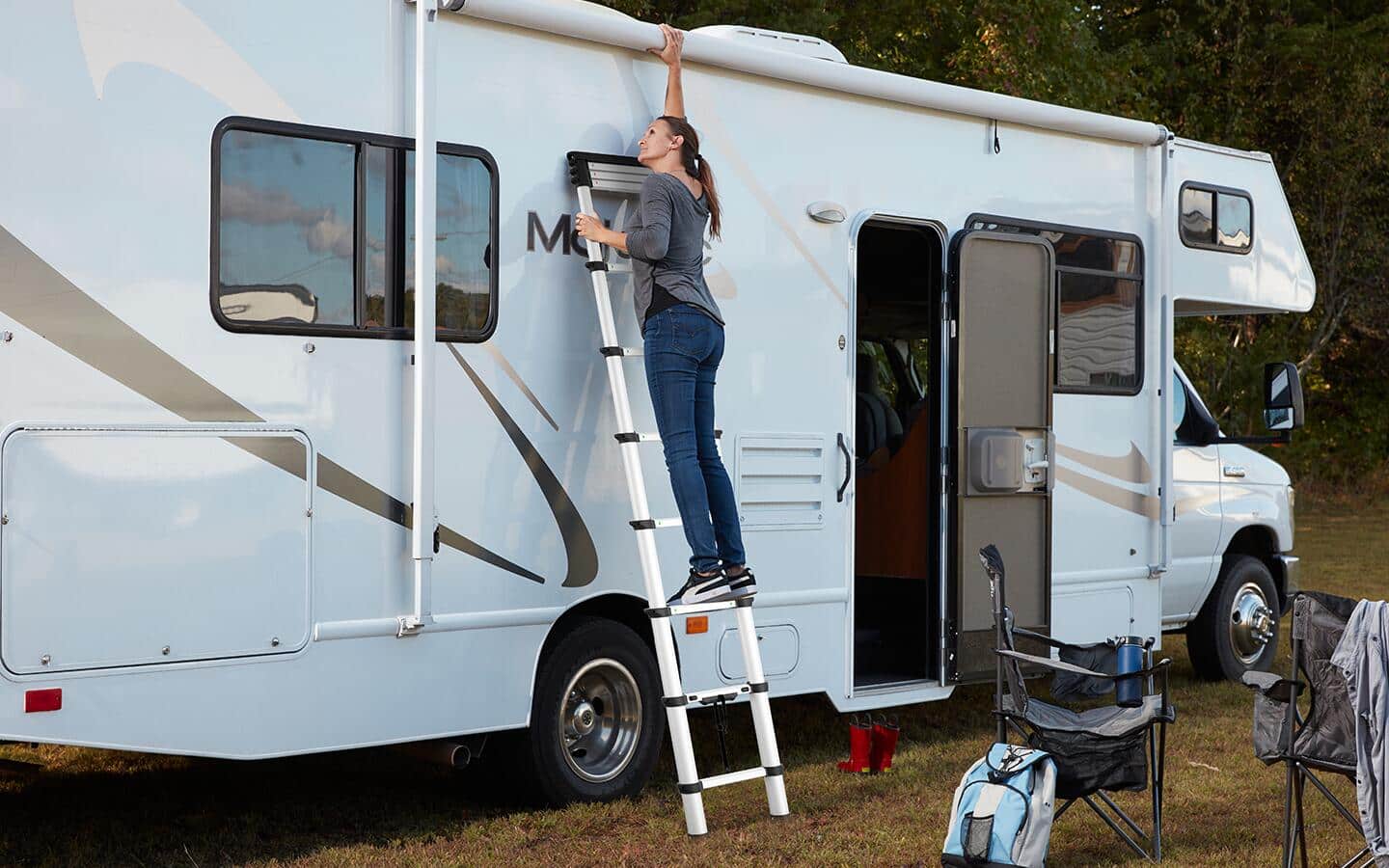 A woman uses a telescoping ladder to reach the awning on an RV.