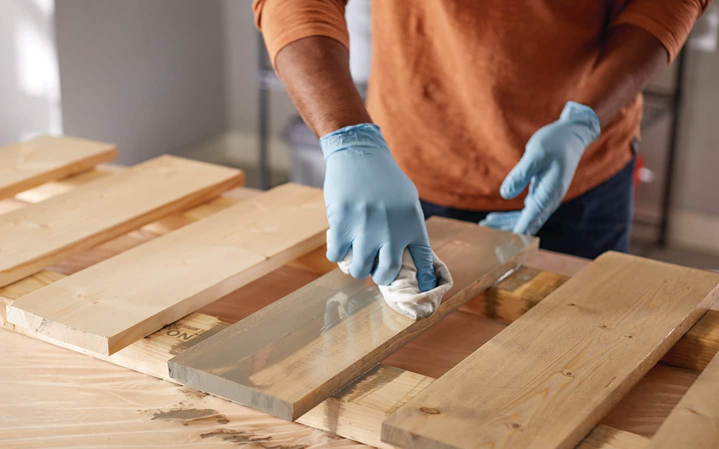 A person in gloves staining a board.