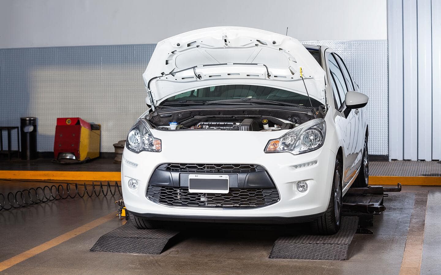 A white vehicle in a shop with the hood open. A white vehicle in a shop with the hood open.