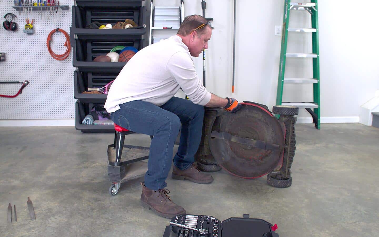 A person tilts a lawn mower on its side to inspect the blade. A person tilts a lawn mower on its side to inspect the blade.