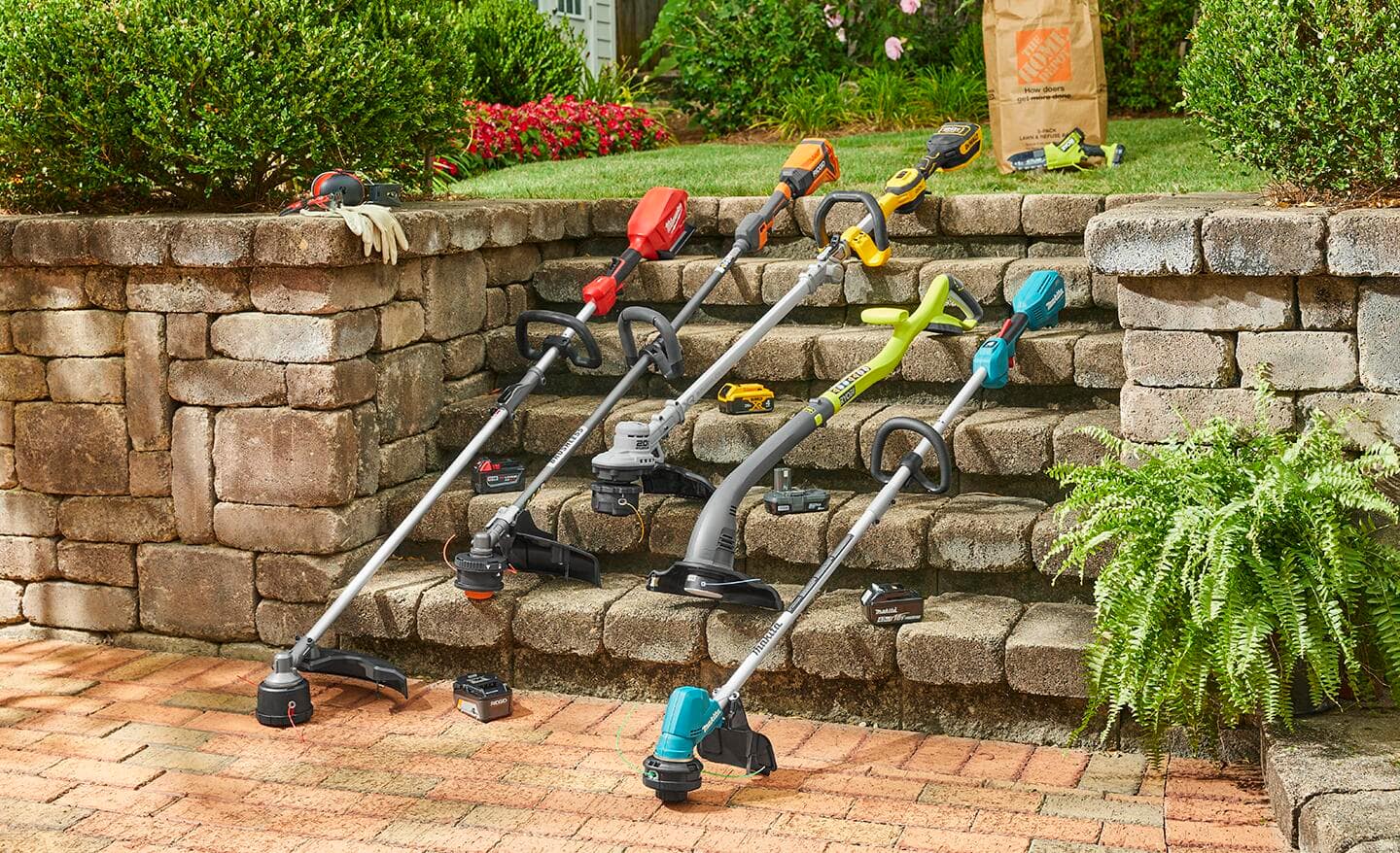 Five different string trimmers of various colors and types leaned up against outdoor patio steps. 
