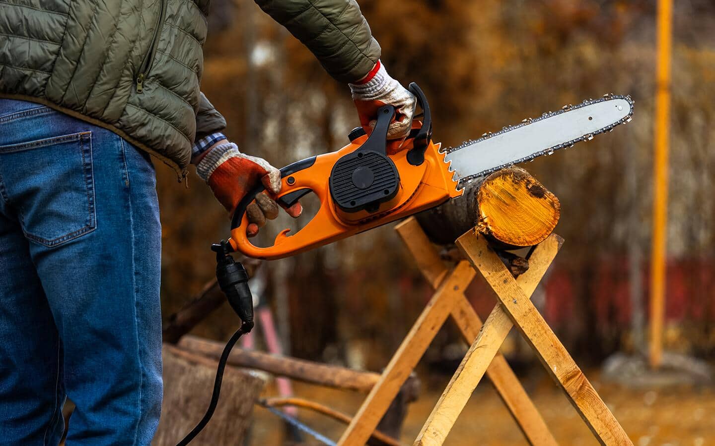 A corded electric chainsaw is used to cut wood on a sawbuck.