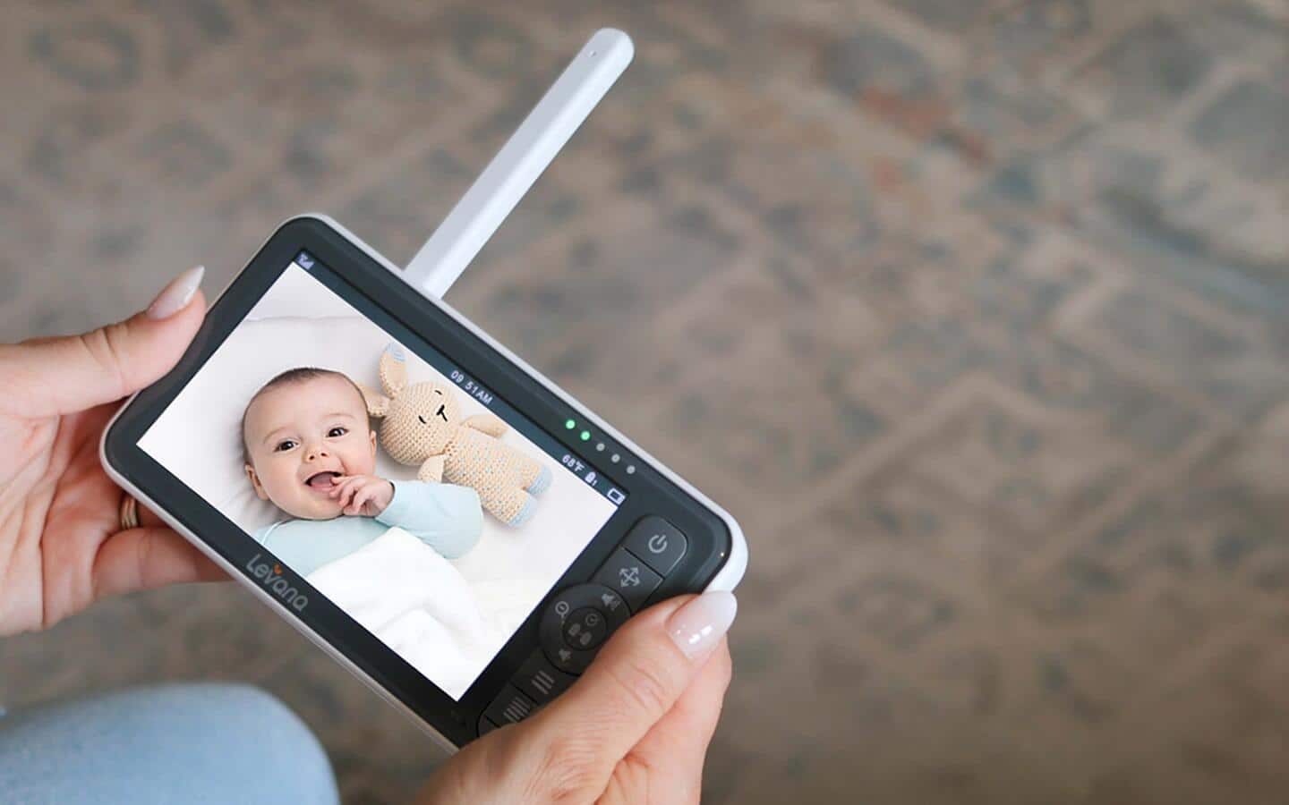 A caretaker holds a mobile device that displays a view from a baby's room.