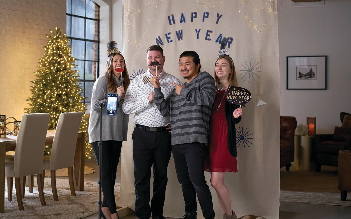 Four people with props photographed in front of a New Year's backdrop of a DIY holiday photo booth. Four people with props photographed in front of a New Year's backdrop of a DIY holiday photo booth.