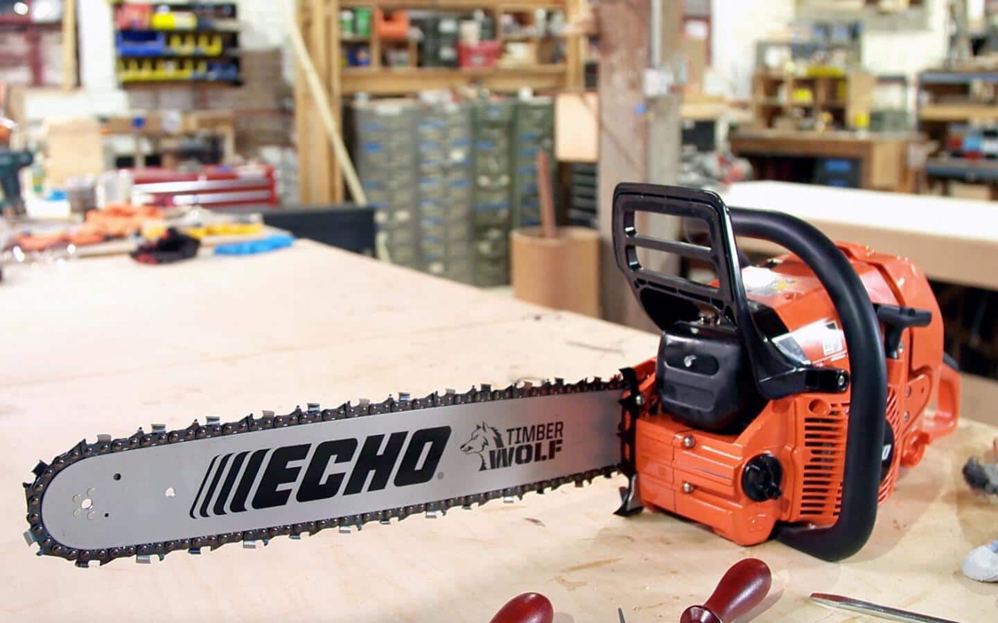 An orange chainsaw lies on a workbench in a woodworking shop. An orange chainsaw lies on a workbench in a woodworking shop.