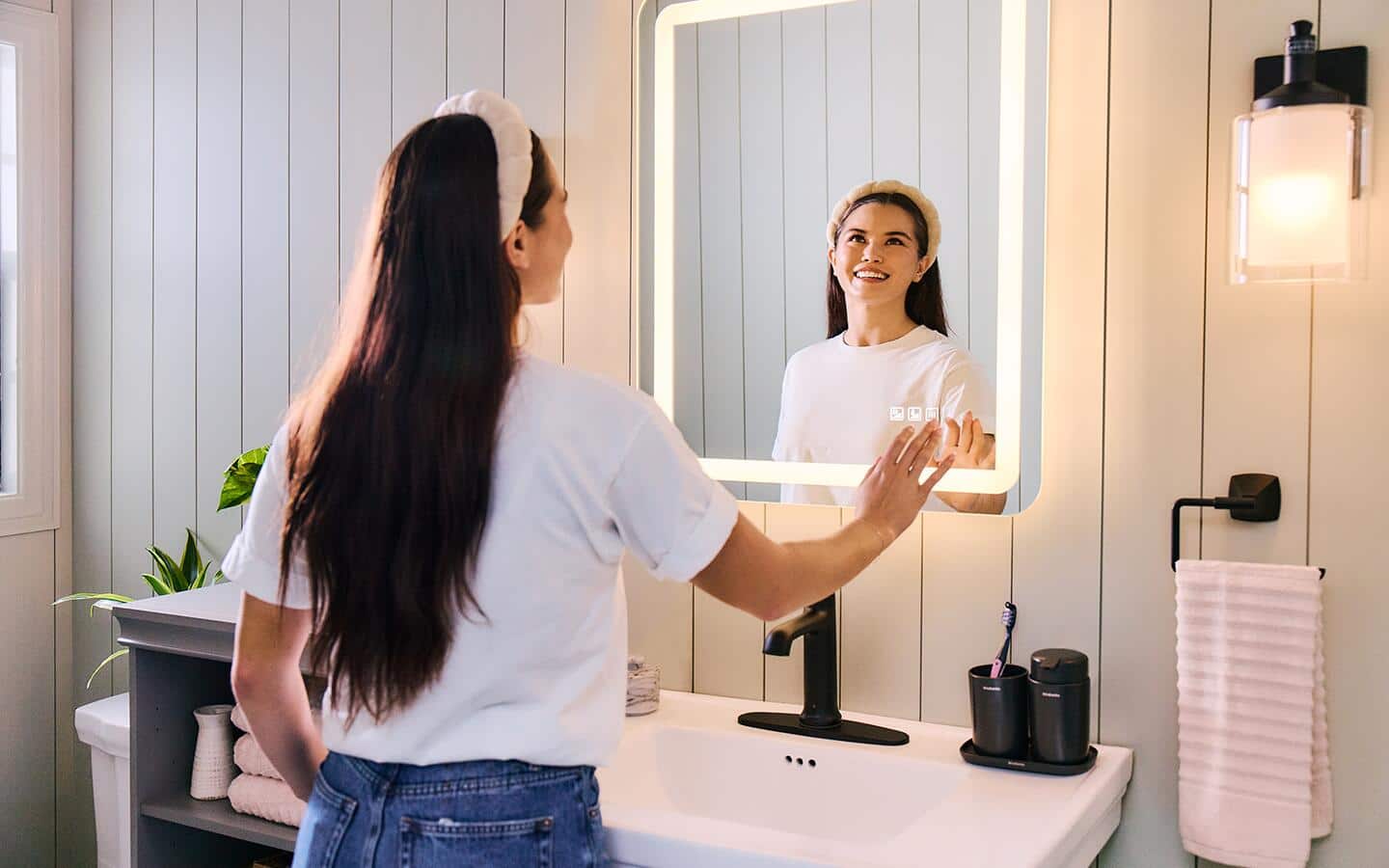 A woman interacting with a smart mirror installed over a bathroom sink.
