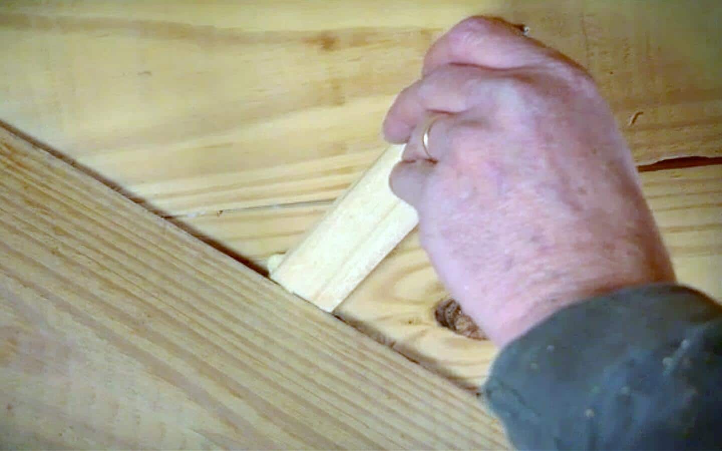 An individual filling a gap in a hardwood floor with a shim.