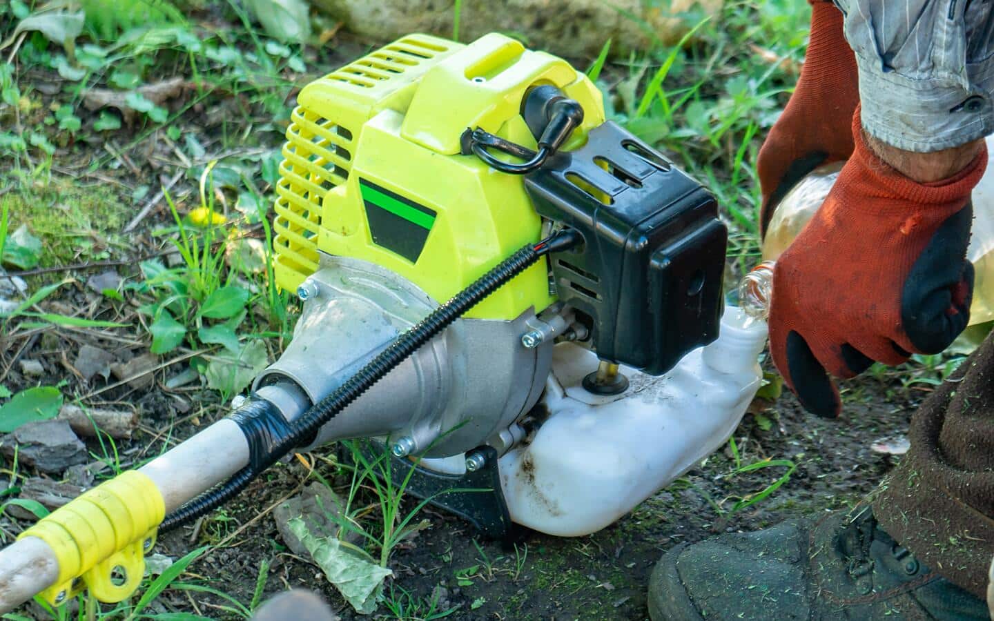 Someone pouring gas into a string trimmer tank.