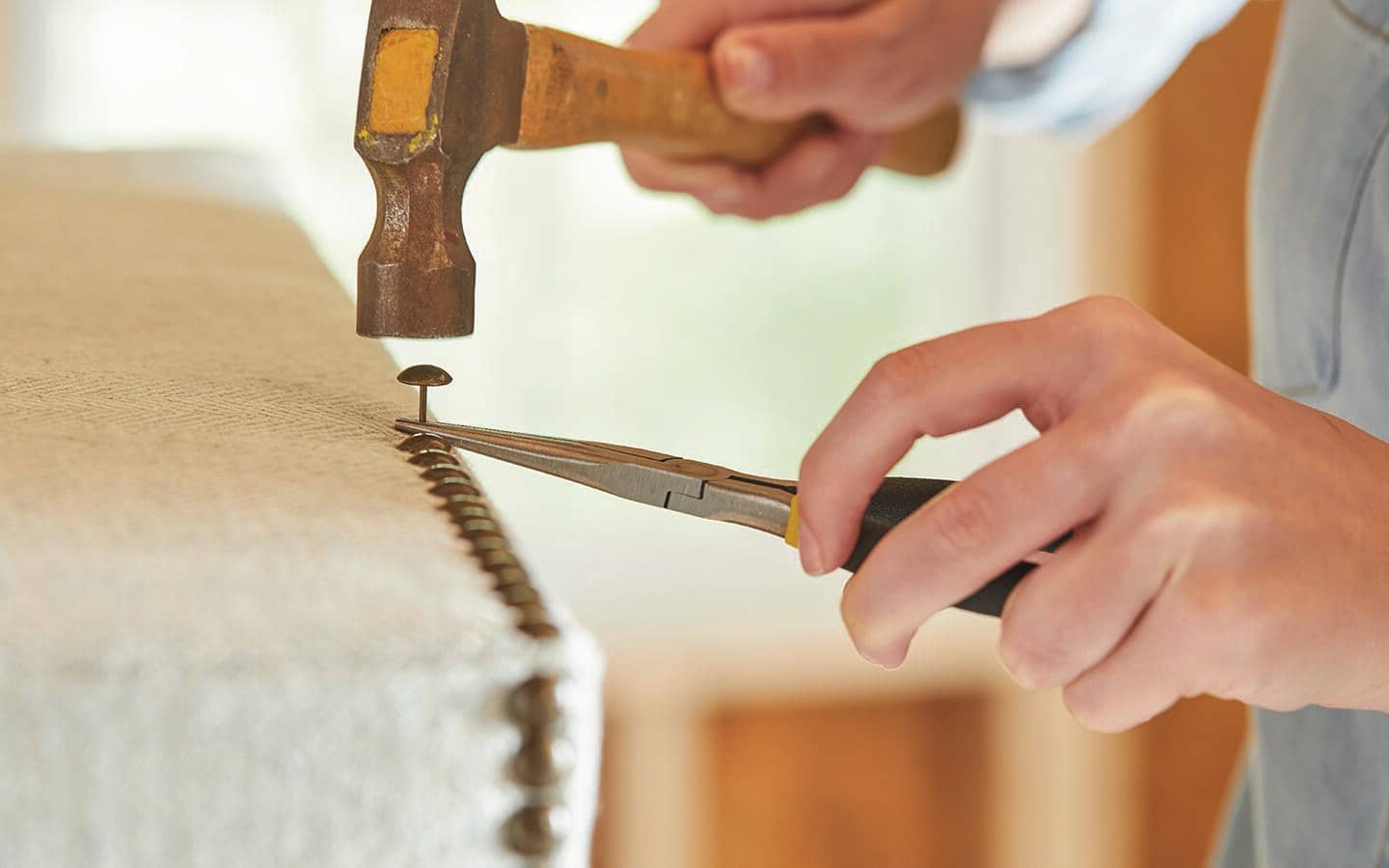 A person uses a hammer to fasten fabric with upholstery tacks. A person uses a hammer to fasten fabric with upholstery tacks.