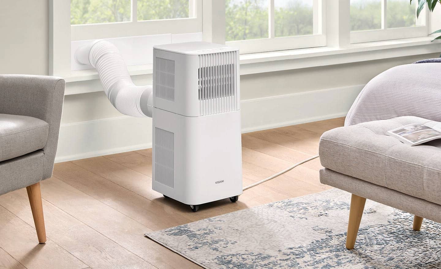 A white, portable air conditioner near a window and between two chairs.