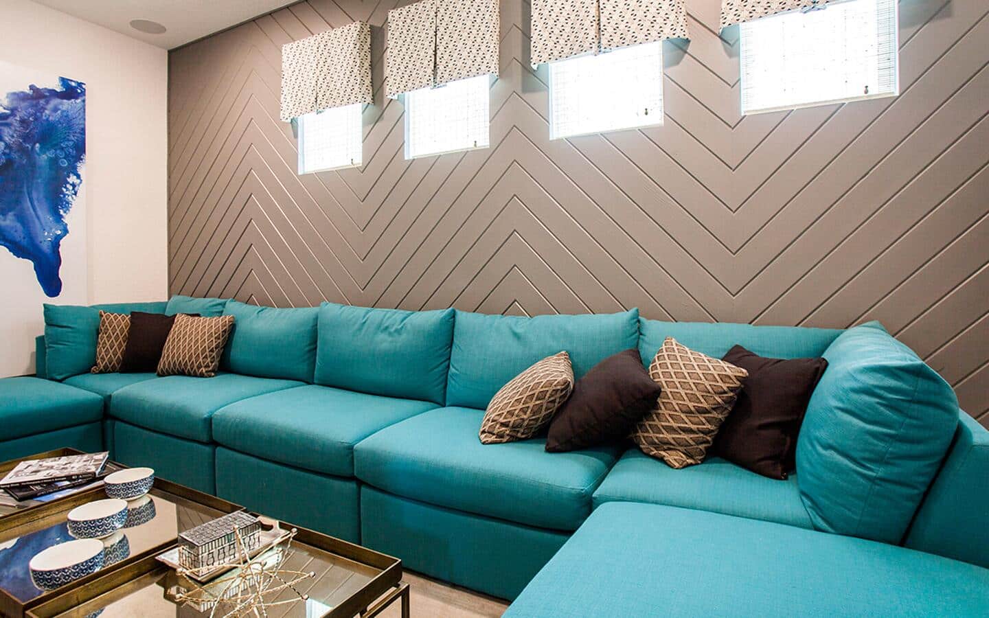 A teal sofa set with brown throw pillows in front of a brown, stenciled accent wall.