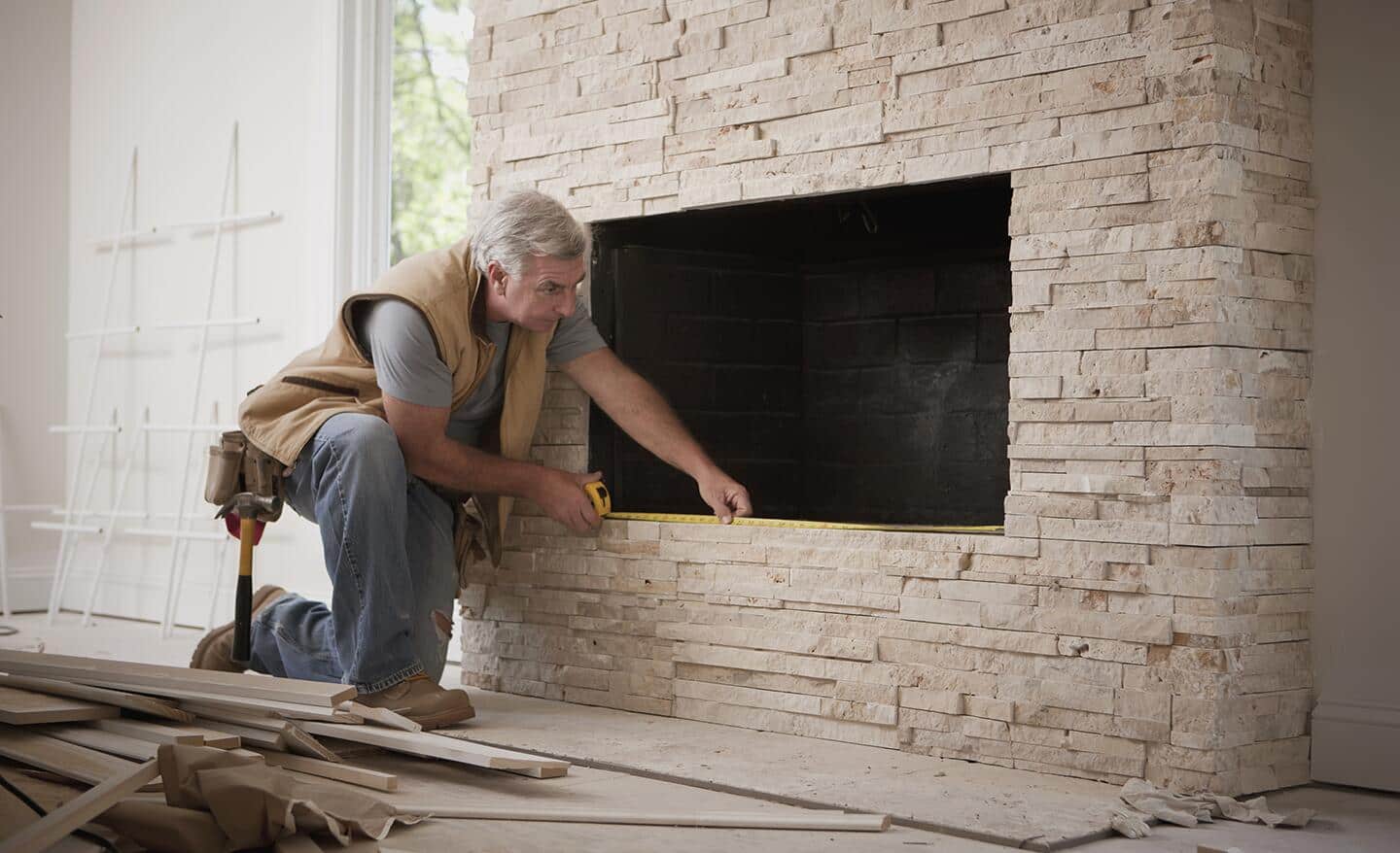 A person uses a measuring tape on a fireplace opening for an insert. A person uses a measuring tape on a fireplace opening for an insert.